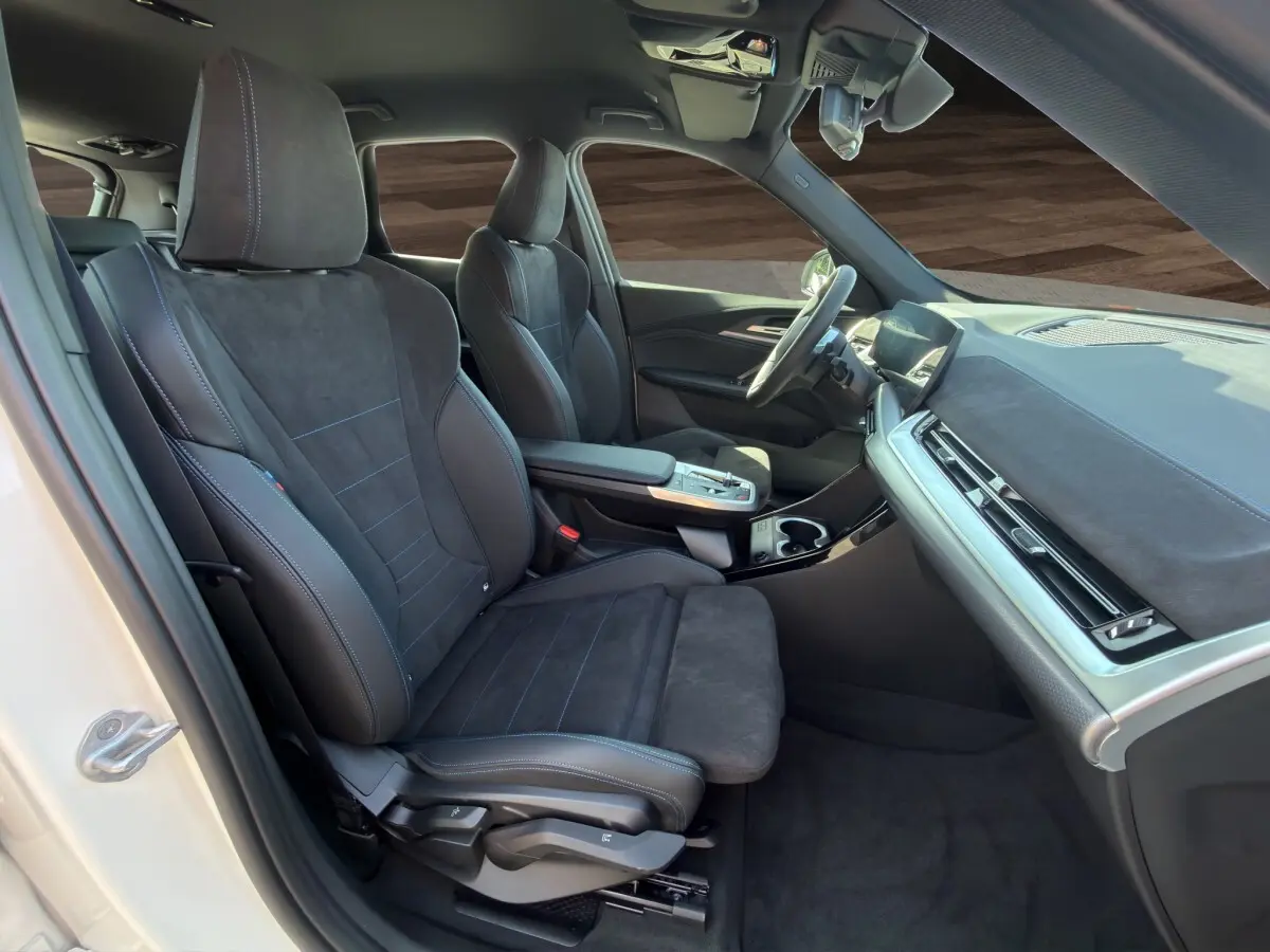 Intérieur avant droit de la BMW X1 blanc 2025, sièges sport noirs avec surpiqûres bleues et tableau de bord moderne.