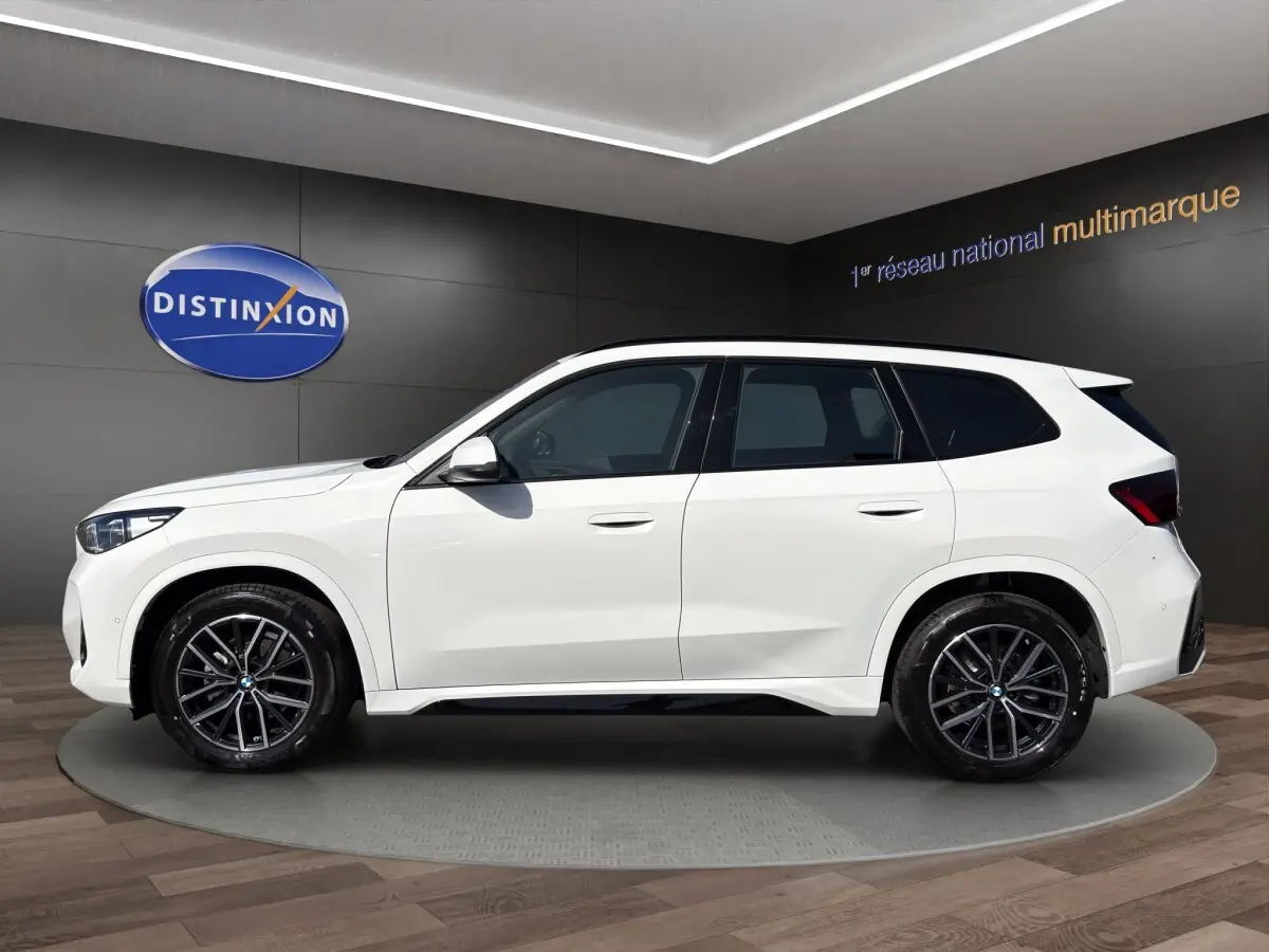 BMW X1 sDrive20d blanc vue de profil côté gauche avec jantes noires en showroom intérieur
