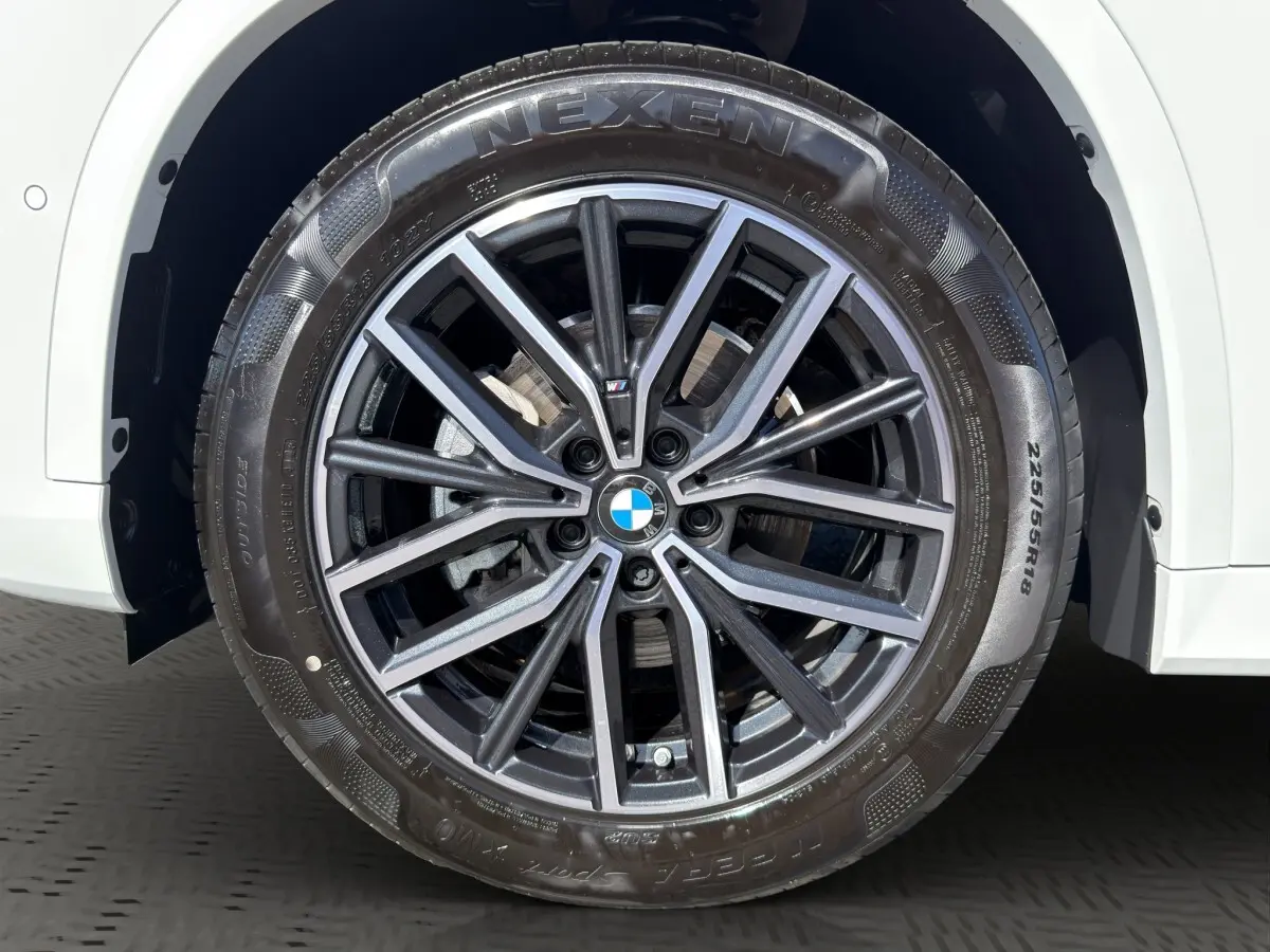 Gros plan sur la roue avant droite d’un BMW X1 blanc avec jante alliage M Sport et pneu Nexen.