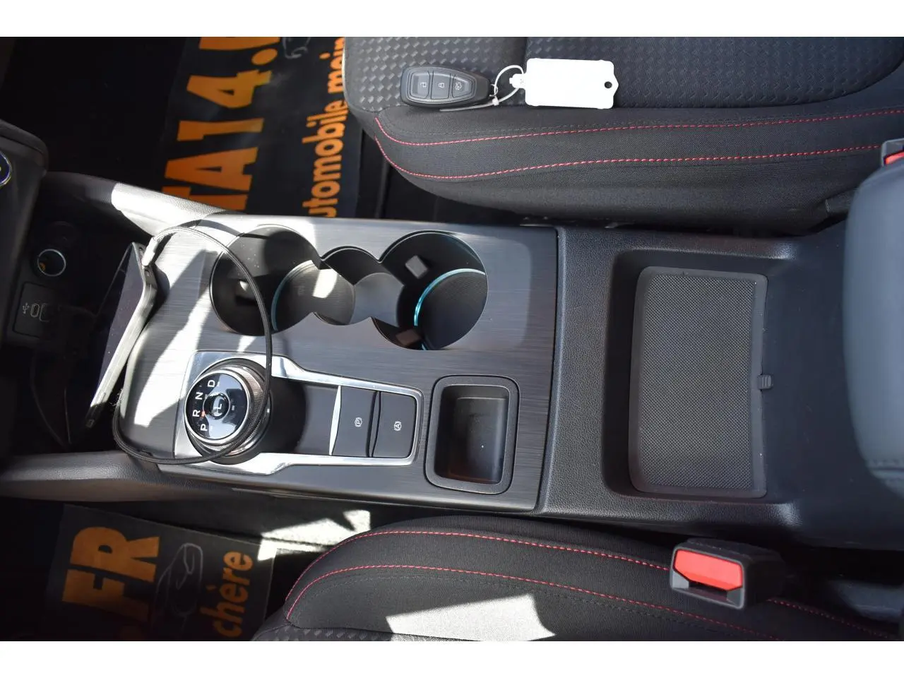Vue plongeante sur la console centrale de la Ford Focus SW Moondust Silver, avec sélecteur rotatif de boîte auto et sièges noirs à surpiqûres rouges.