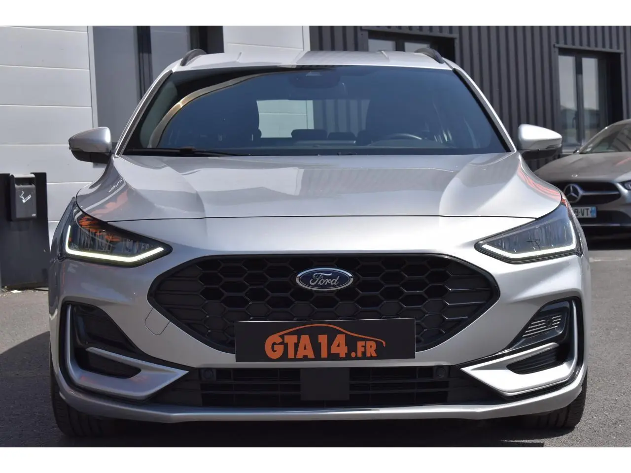 Vue frontale d'une Ford Focus SW 1.5 EcoBlue 115 ST LINE X en Moondust Silver avec calandre noire et feux LED allumés.