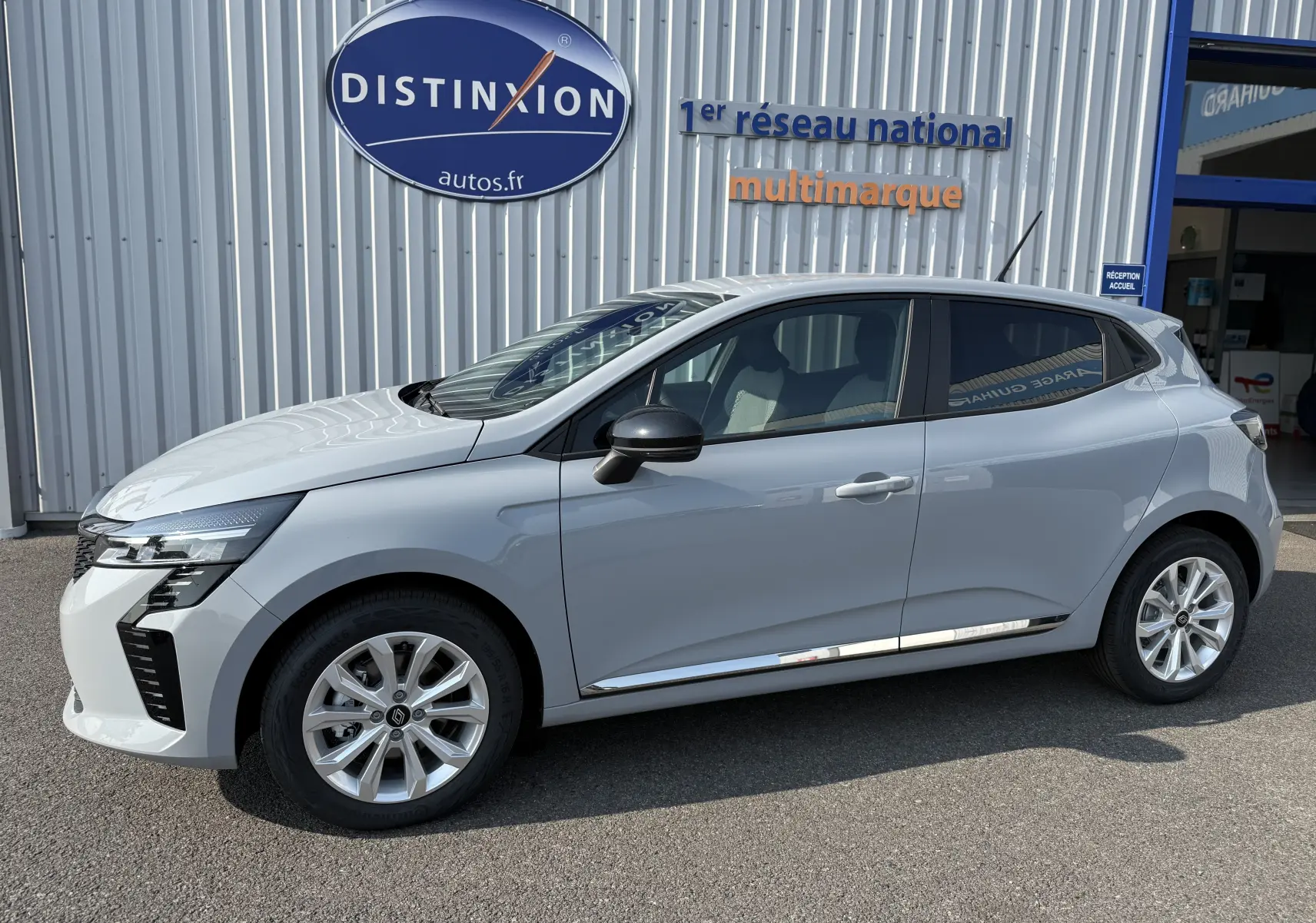 Profil côté gauche de la Renault Clio 1.5 DCI 100ch Evolution gris Rafale Métal, garée devant un bâtiment commercial.