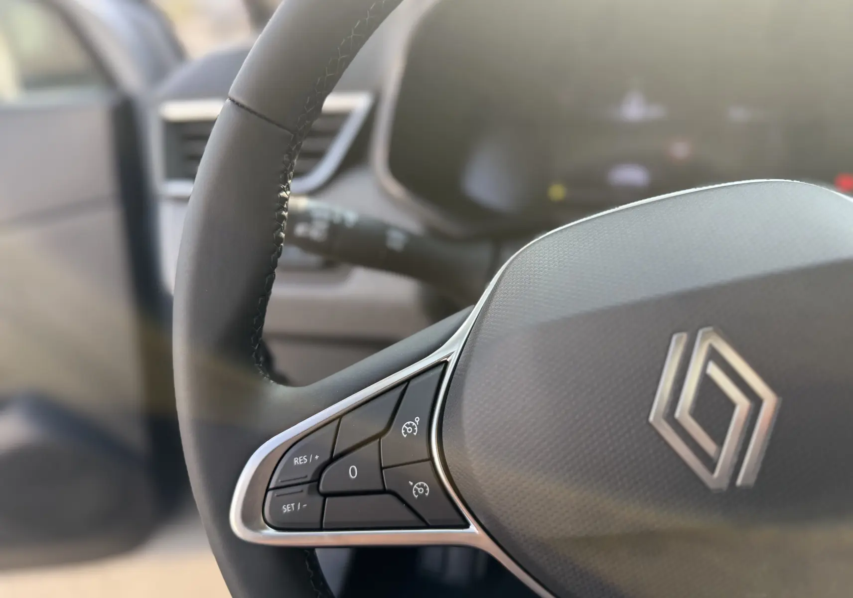 Gros plan sur le volant gris foncé de la Renault Clio 2025 avec commandes intégrées et logo au centre.