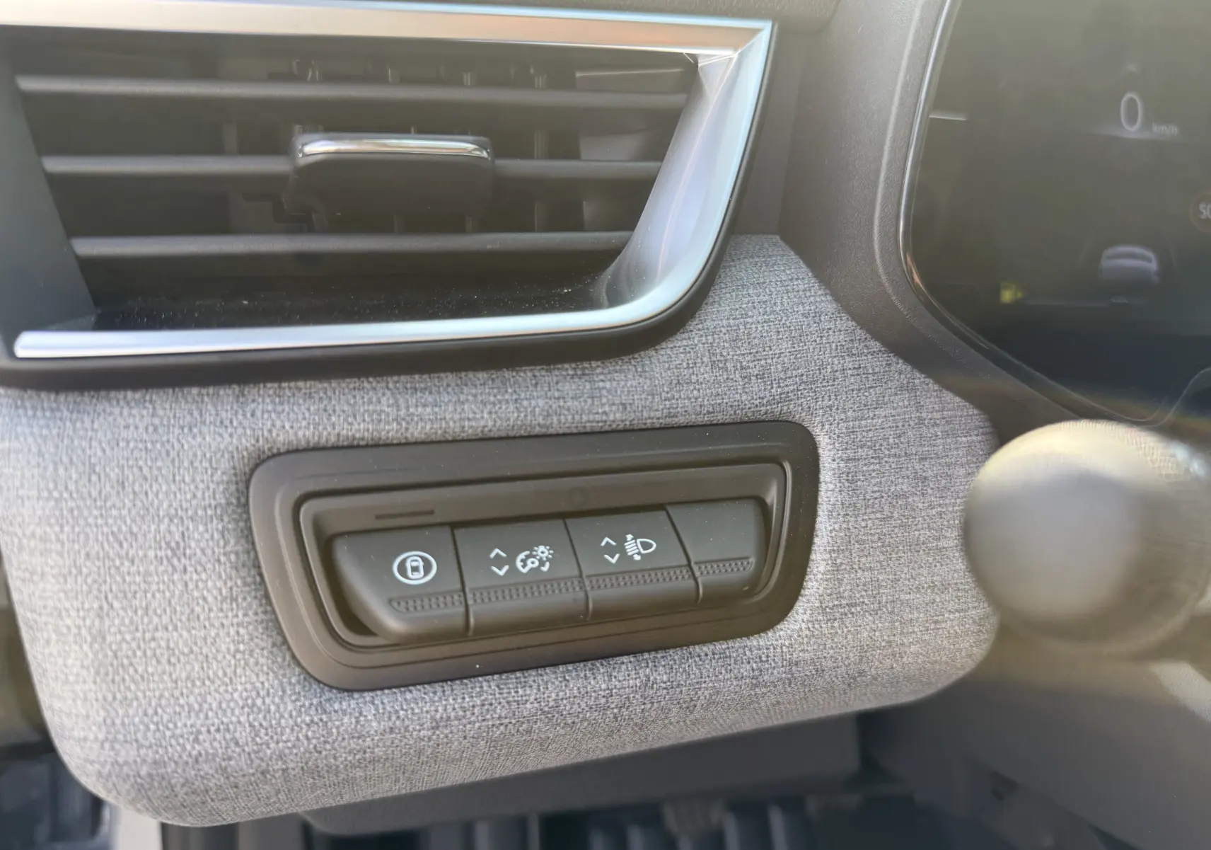 Détail du tableau de bord gris clair de la Renault Clio 2025 montrant les commandes d'éclairage et verrouillage sous la grille d'aération.