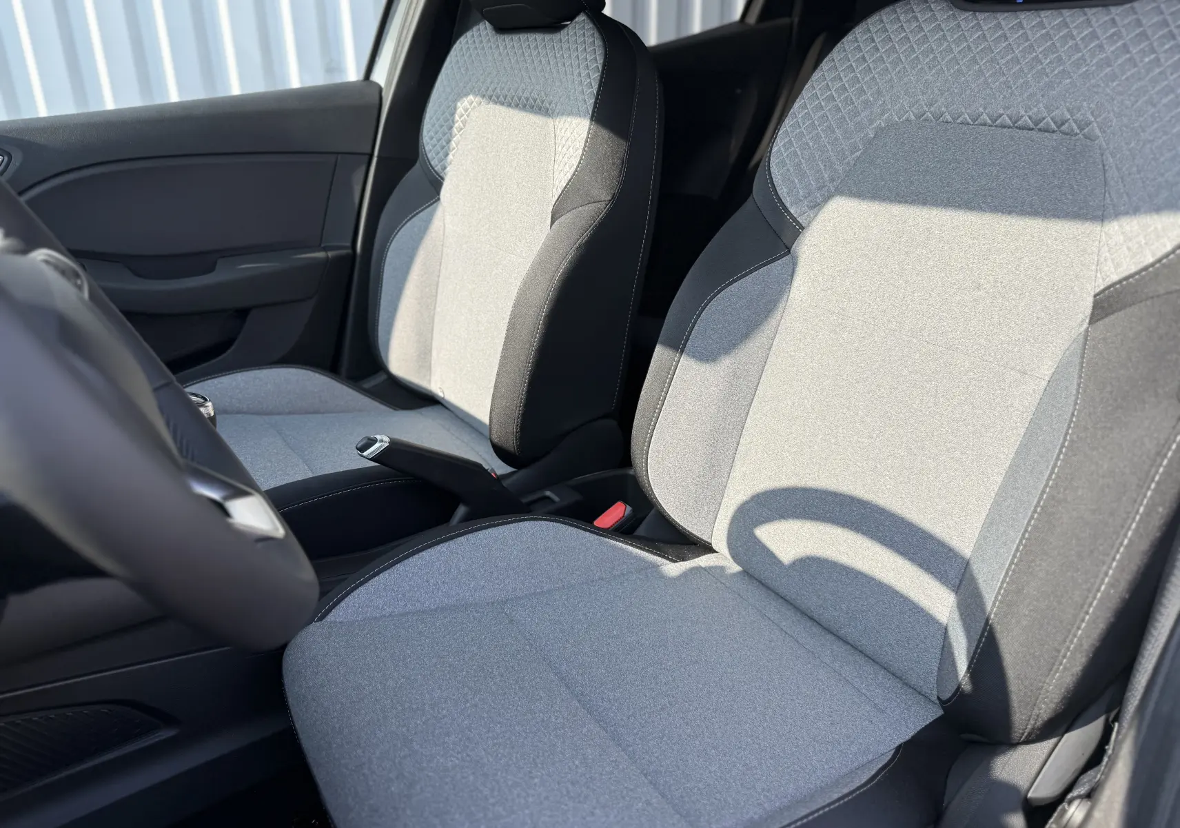 Vue rapprochée des sièges avant gris clair et noirs de la Renault Clio 1.5 DCI 100CH Evolution 2025, intérieur lumineux.