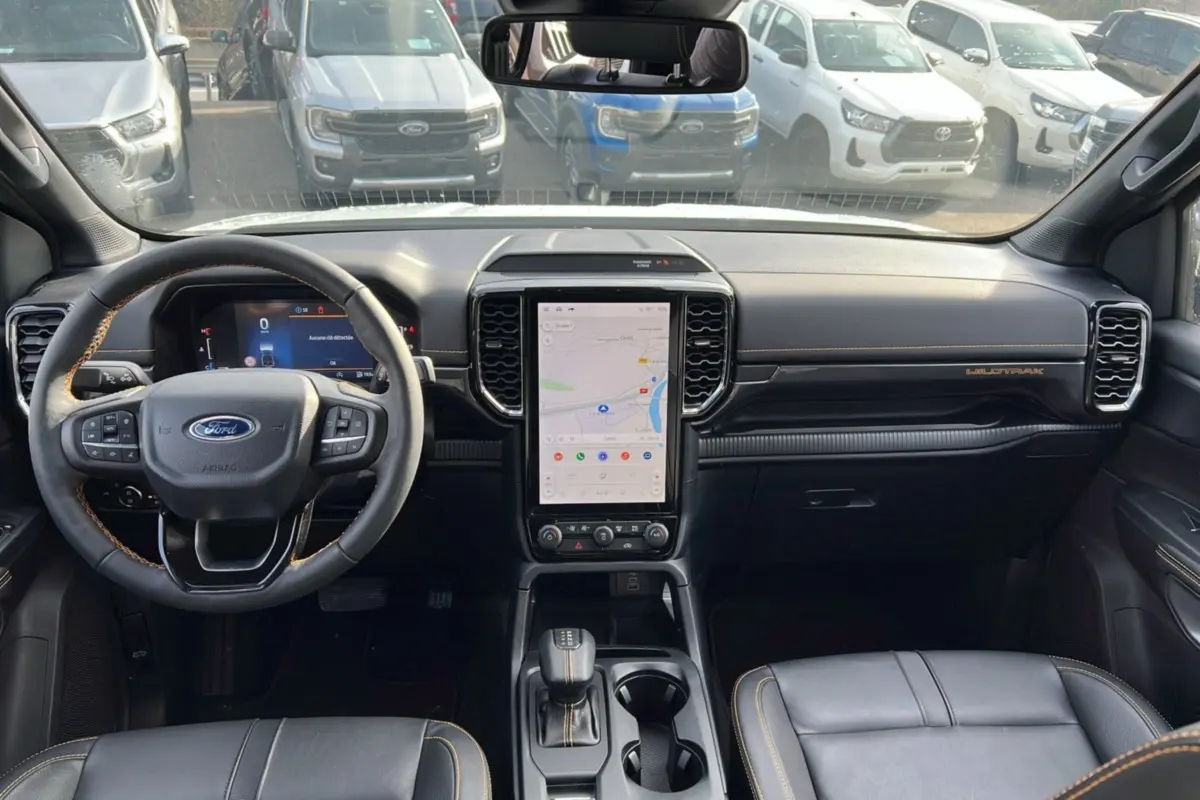 Vue intérieure avant du Ford Ranger Wildtrak 2025, tableau de bord noir avec écran tactile vertical et volant cuir noir.