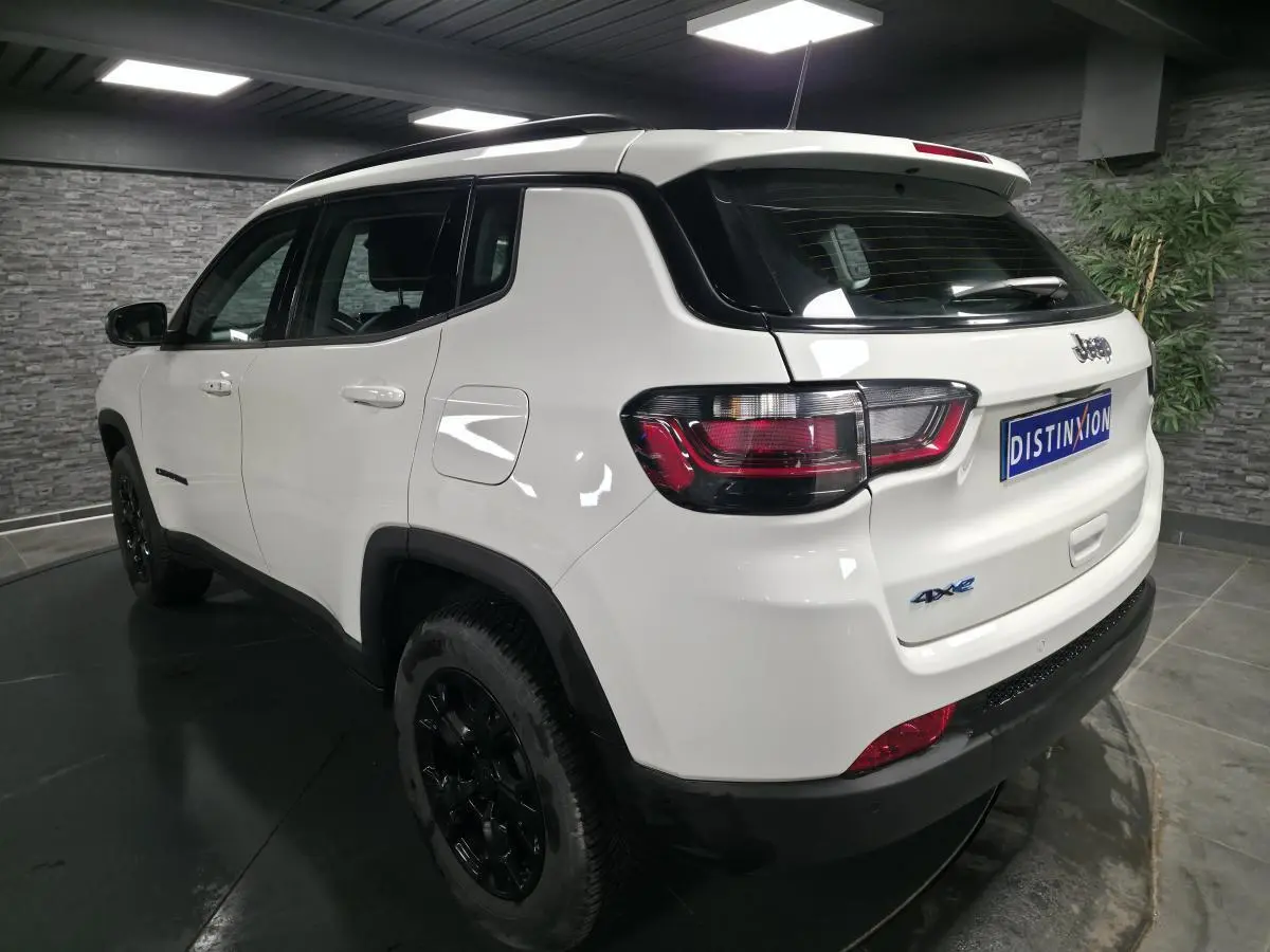 Jeep Compass blanc vue 3/4 arrière droit avec jantes noires et badges 4xe eAWD visibles.