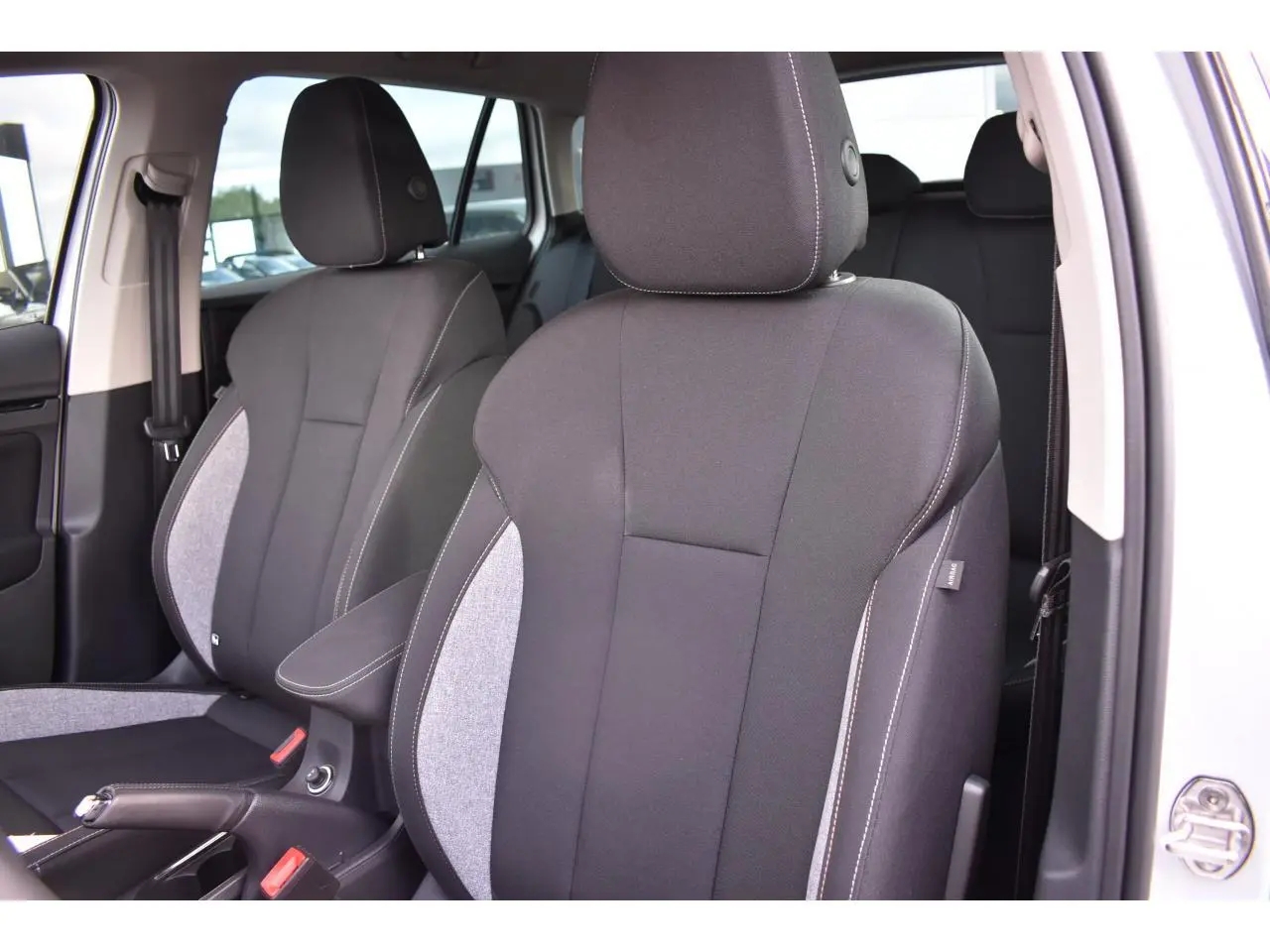Vue rapprochée des sièges avant en tissu noir et gris du Skoda Scala blanc glacier, porte ouverte côté droit.
