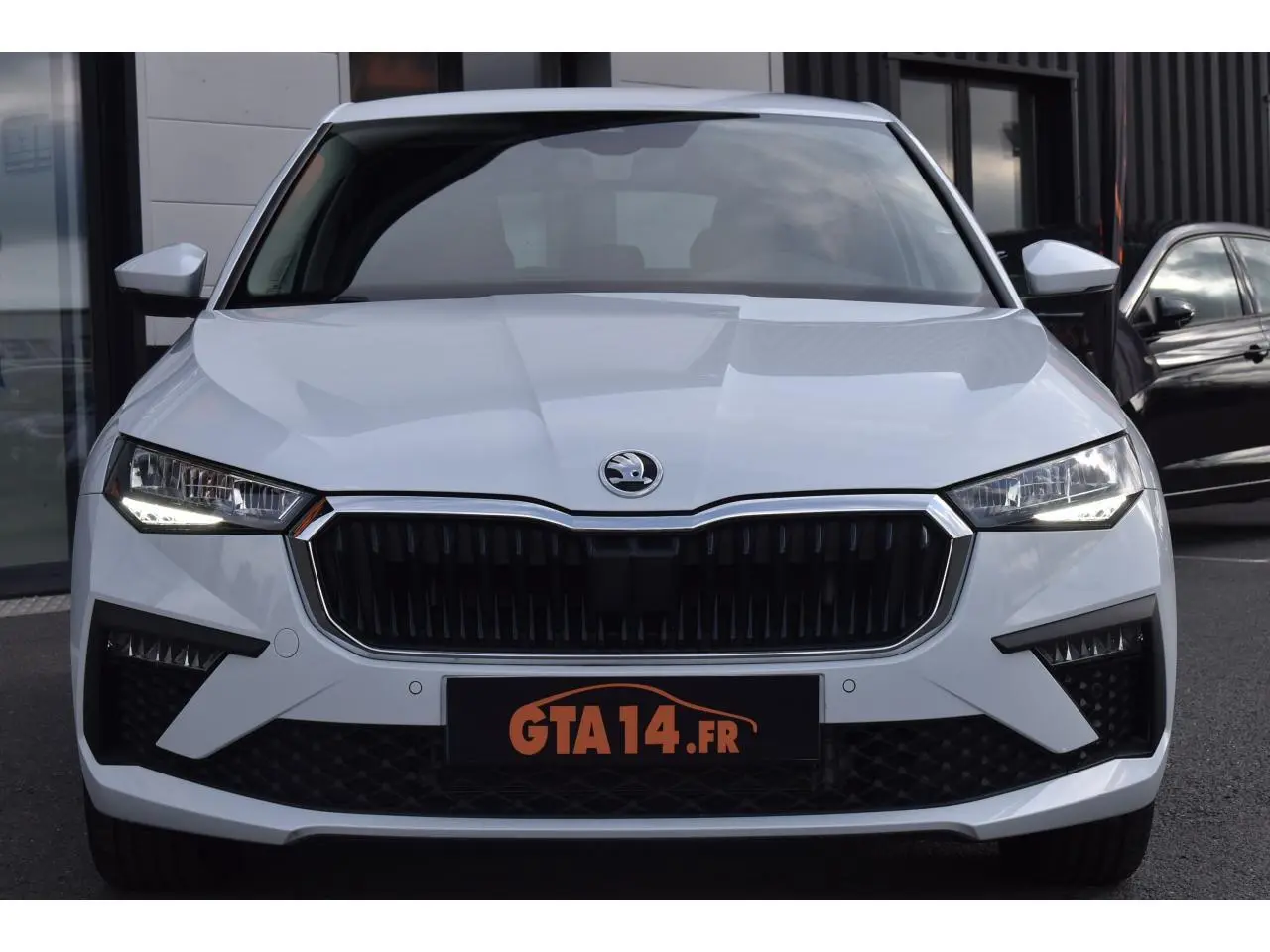 Vue avant d'une Skoda Scala blanc glacier avec calandre noire et feux LED allumés sur parking urbain.