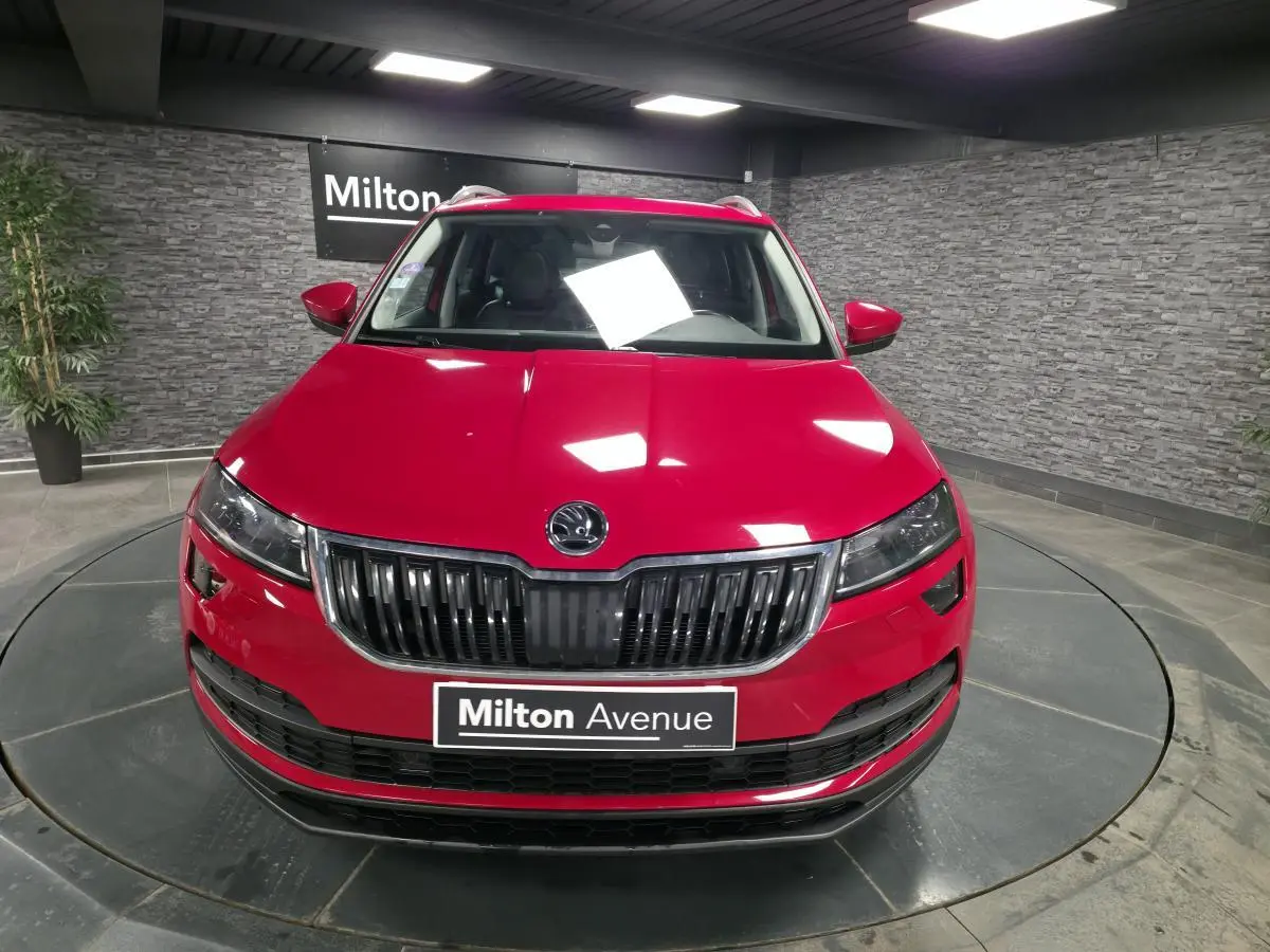 Vue frontale d'un Skoda Karoq rouge brillant avec calandre noire et plaque Milton Avenue en intérieur showroom.