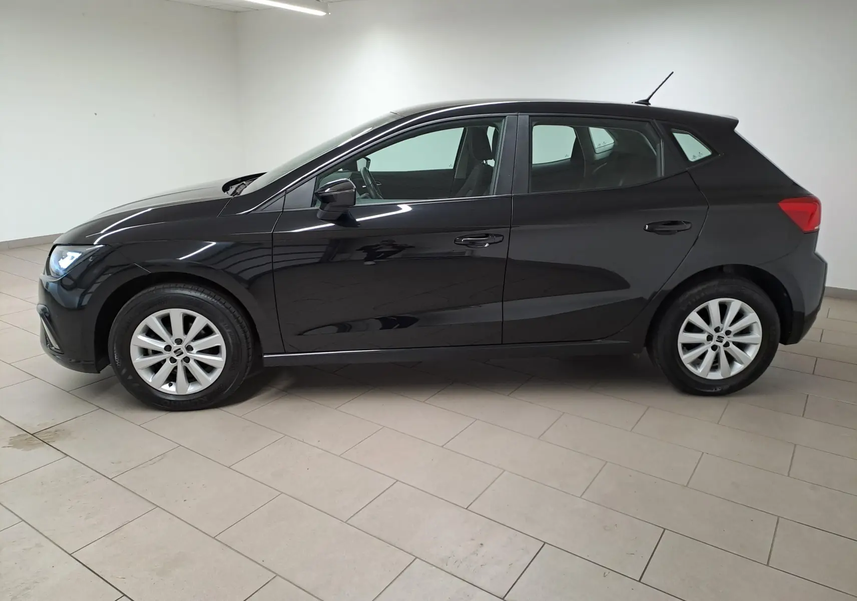 SEAT IBIZA 1.0 TSI 95 STYLE 2024 en noir minuit, vue de profil côté gauche dans un intérieur lumineux.