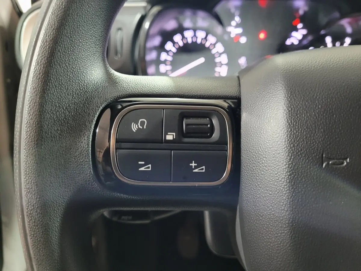 Gros plan sur les commandes gauche du volant noir de la Citroën C3 2022, avec tableau de bord flou en arrière-plan.