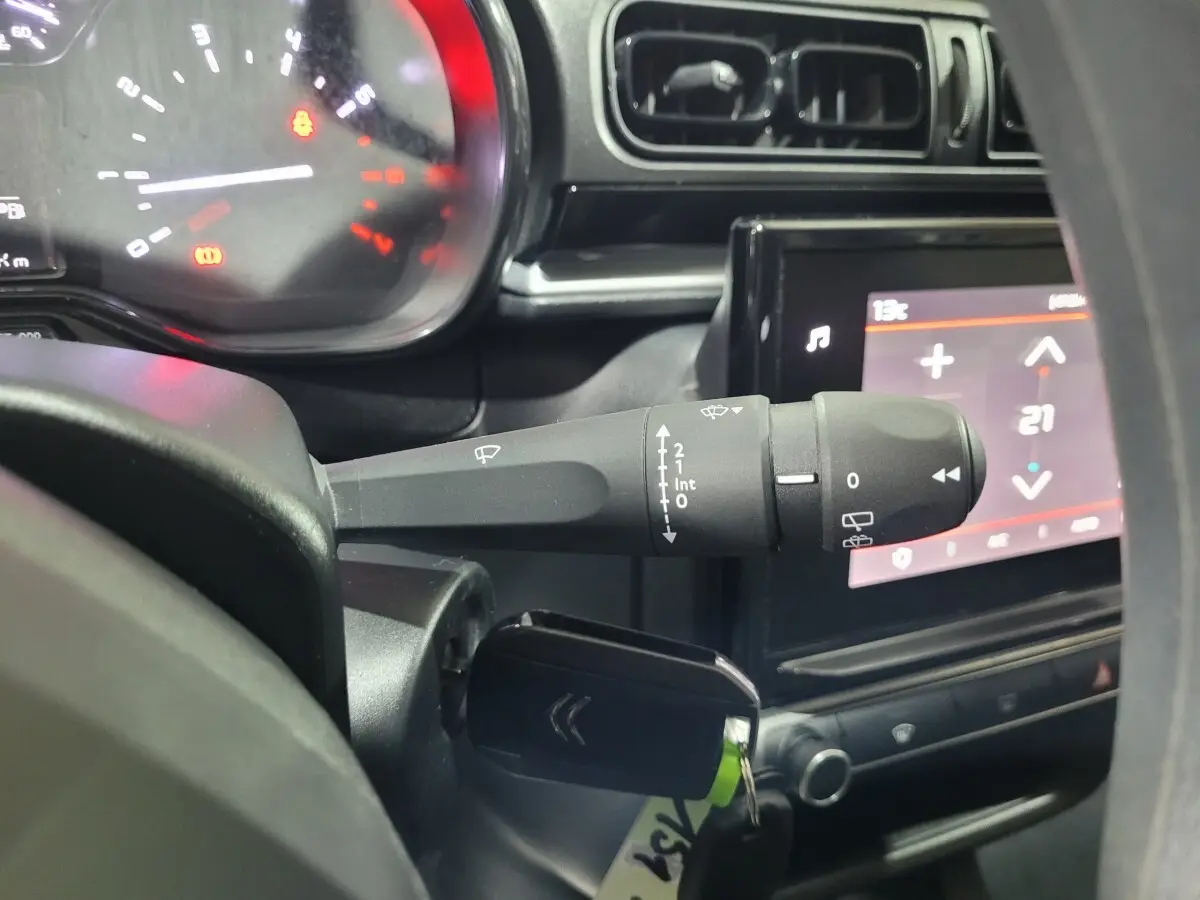 Gros plan intérieur sur la commande d’essuie-glaces à gauche du volant d’une Citroën C3 beige, avec tableau de bord et écran tactile visible.