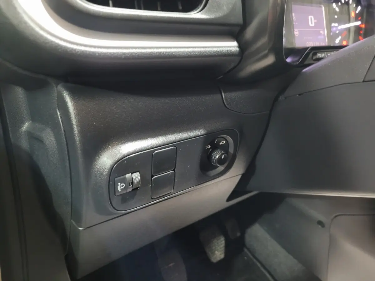 Gros plan sur les commandes d'éclairage et réglage des phares à gauche du tableau de bord de la Citroën C3 beige.