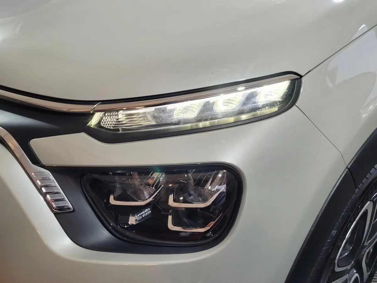 Gros plan sur le phare avant droit allumé d'une Citroën C3 beige 2022 avec signature lumineuse LED distinctive.