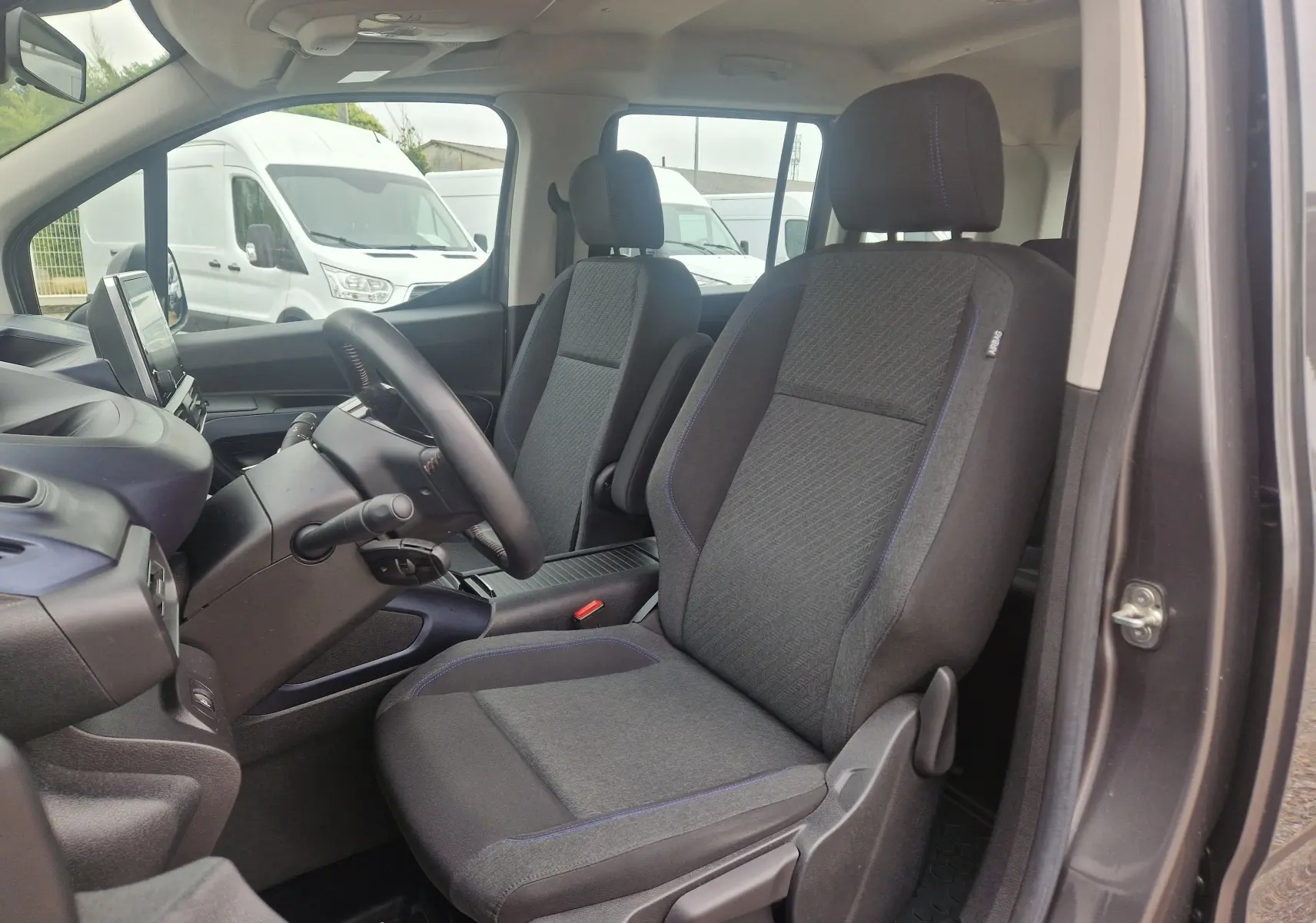 Vue intérieure côté conducteur du Peugeot Rifter gris platinium, mettant en valeur les sièges tissu et le tableau de bord moderne.