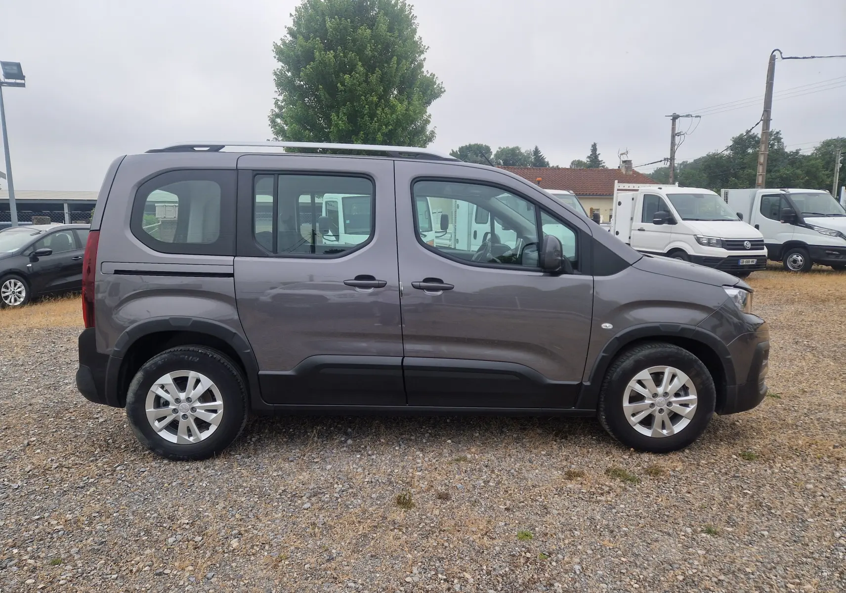 Profil côté gauche du Peugeot Rifter gris platinium 2019 avec jantes alliage et barres de toit visibles.