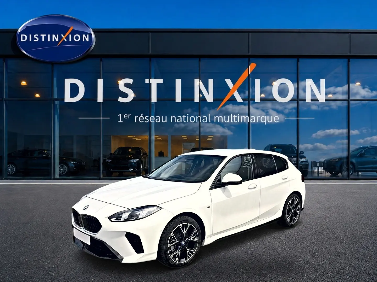 BMW Série 1 blanche vue en 3/4 avant droit, avec jantes alliage noires et calandre M Sport devant un showroom Distinxion.