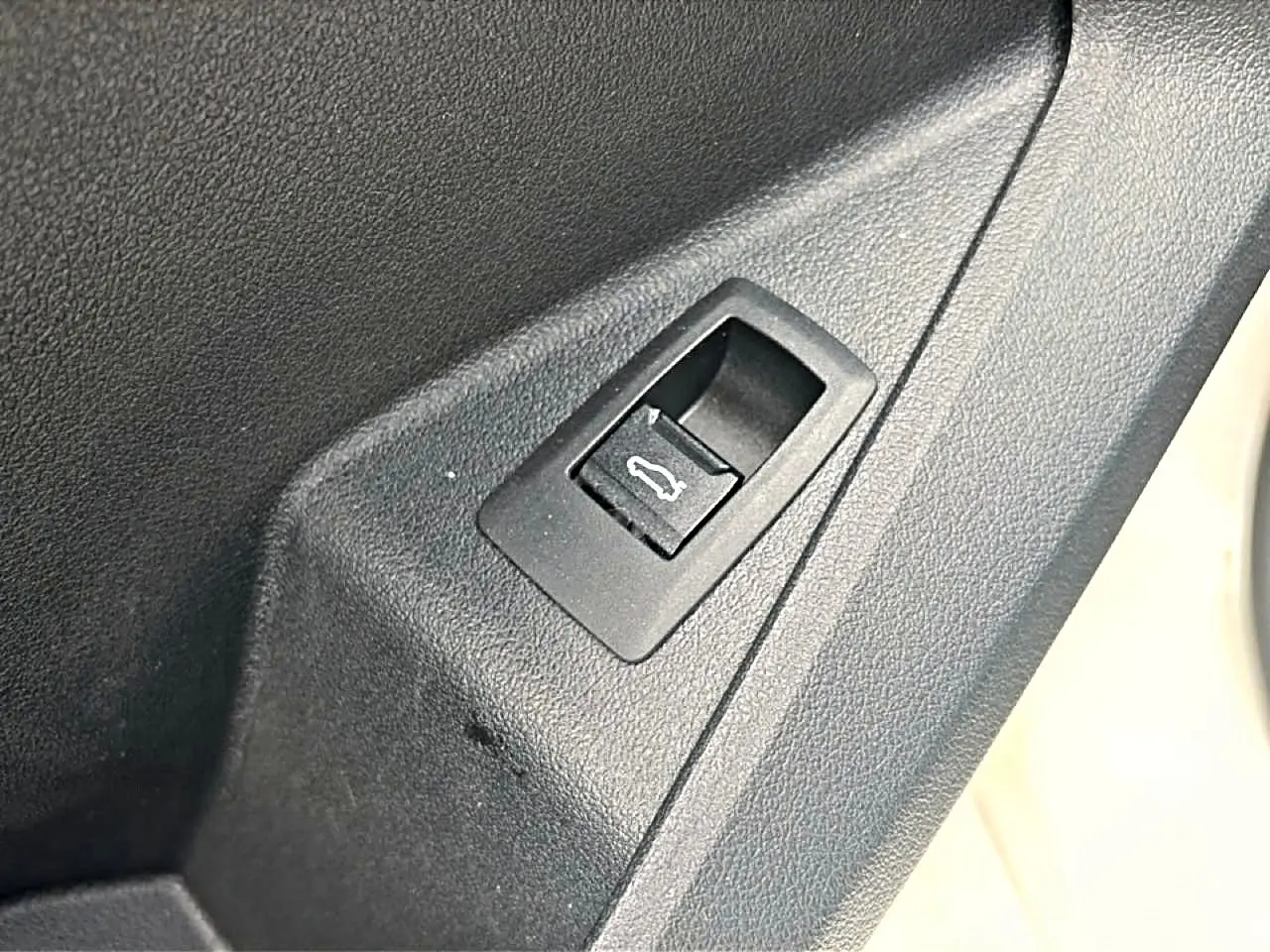 Gros plan sur le bouton d'ouverture du coffre intégré dans le panneau de porte intérieur noir.