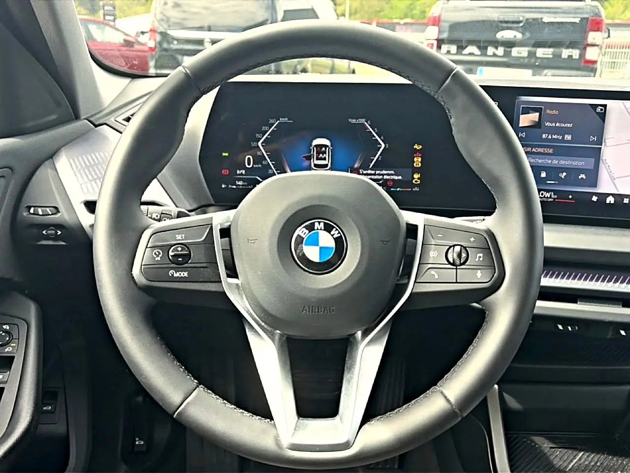 Vue centrée sur le volant cuir noir de la BMW Série 1 120da 2025 avec tableau de bord numérique et écran tactile.