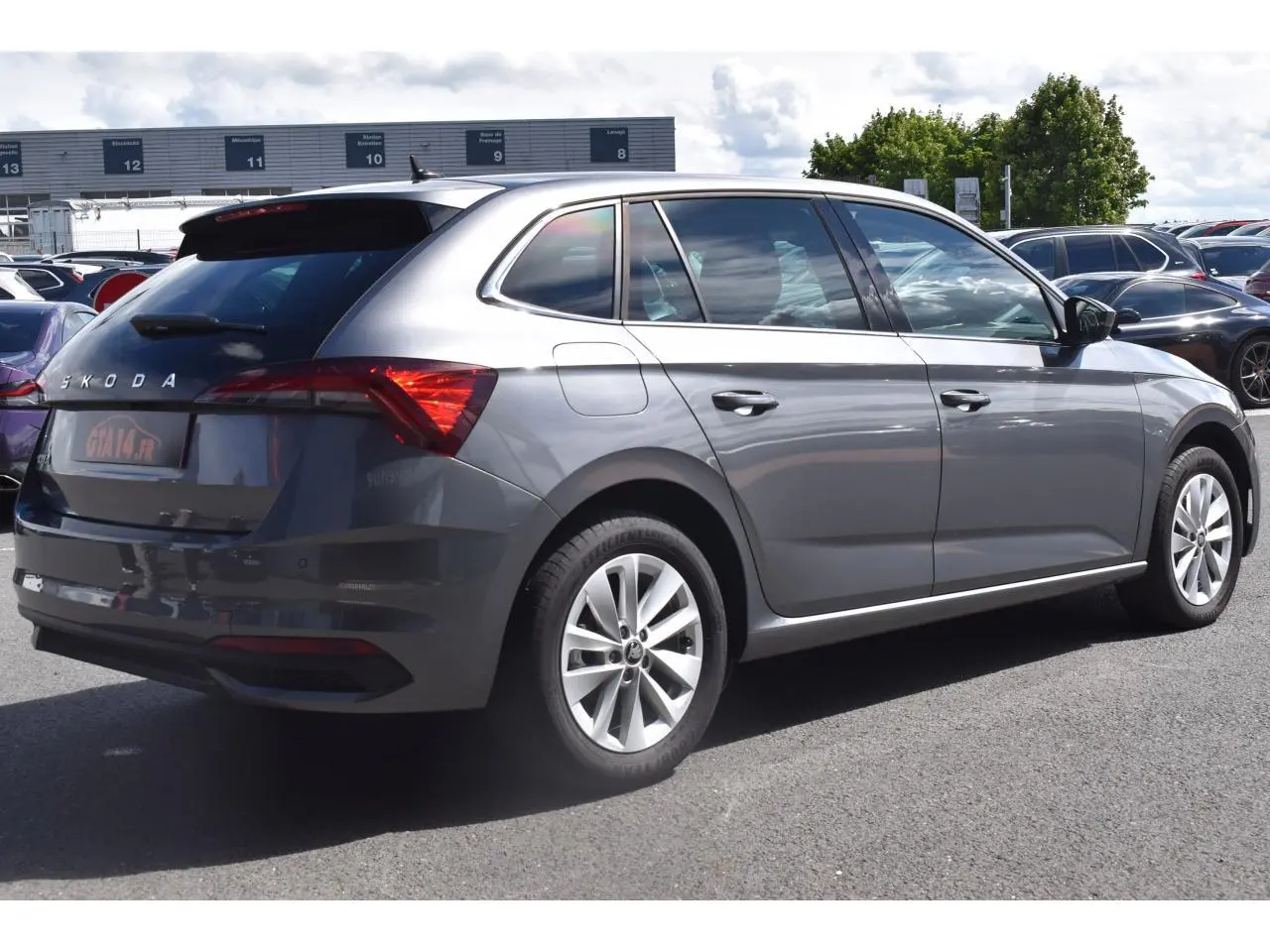 Vue 3/4 arrière droite d'une Skoda Scala gris graphite avec jantes alliage 16 pouces sur parking extérieur.