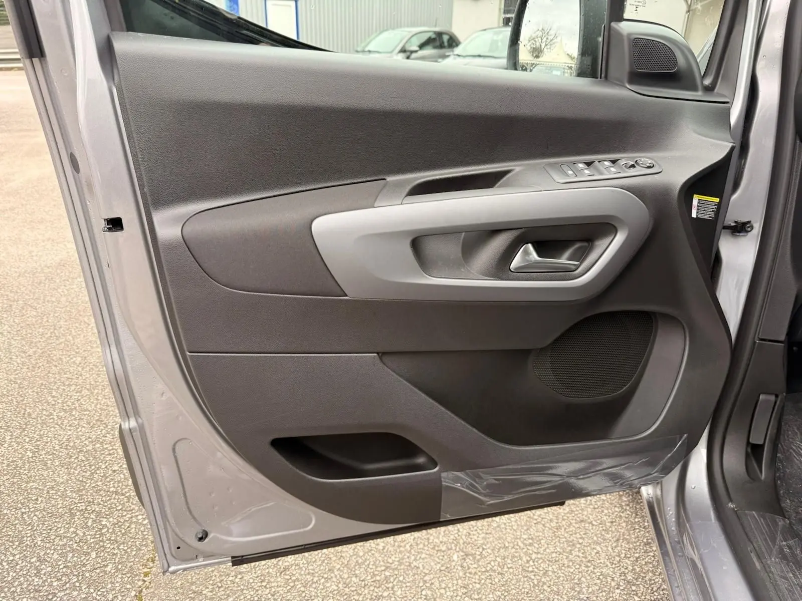 Vue intérieure de la porte avant gauche du Citroën Berlingo gris Artense, avec commandes électriques et haut-parleur intégré.