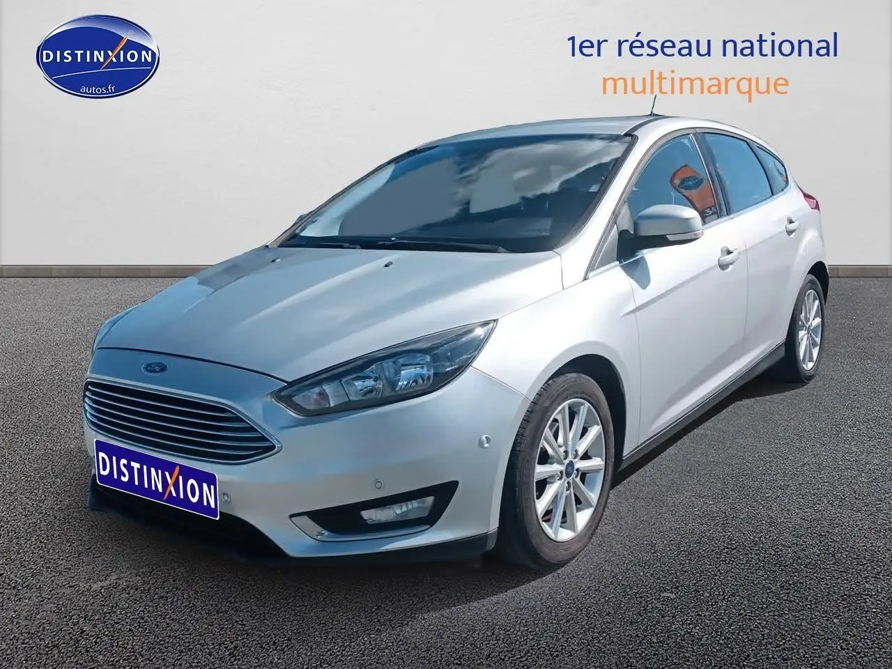 Ford Focus gris clair vue 3/4 avant droit sur parking avec calandre chromée et jantes alu