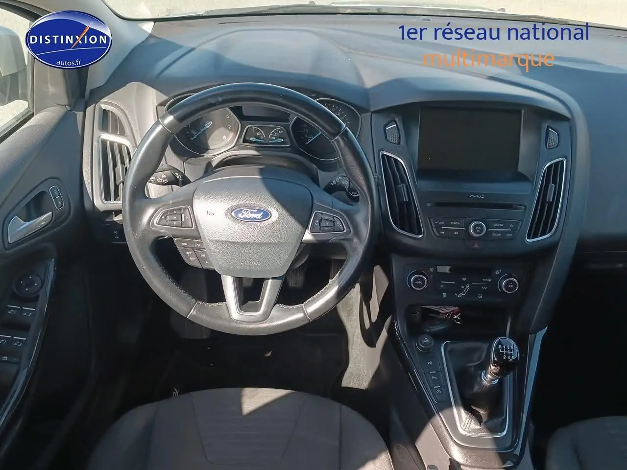 Vue intérieure centrée sur le volant cuir multifonction et la console centrale d'une Ford Focus gris clair 2017.
