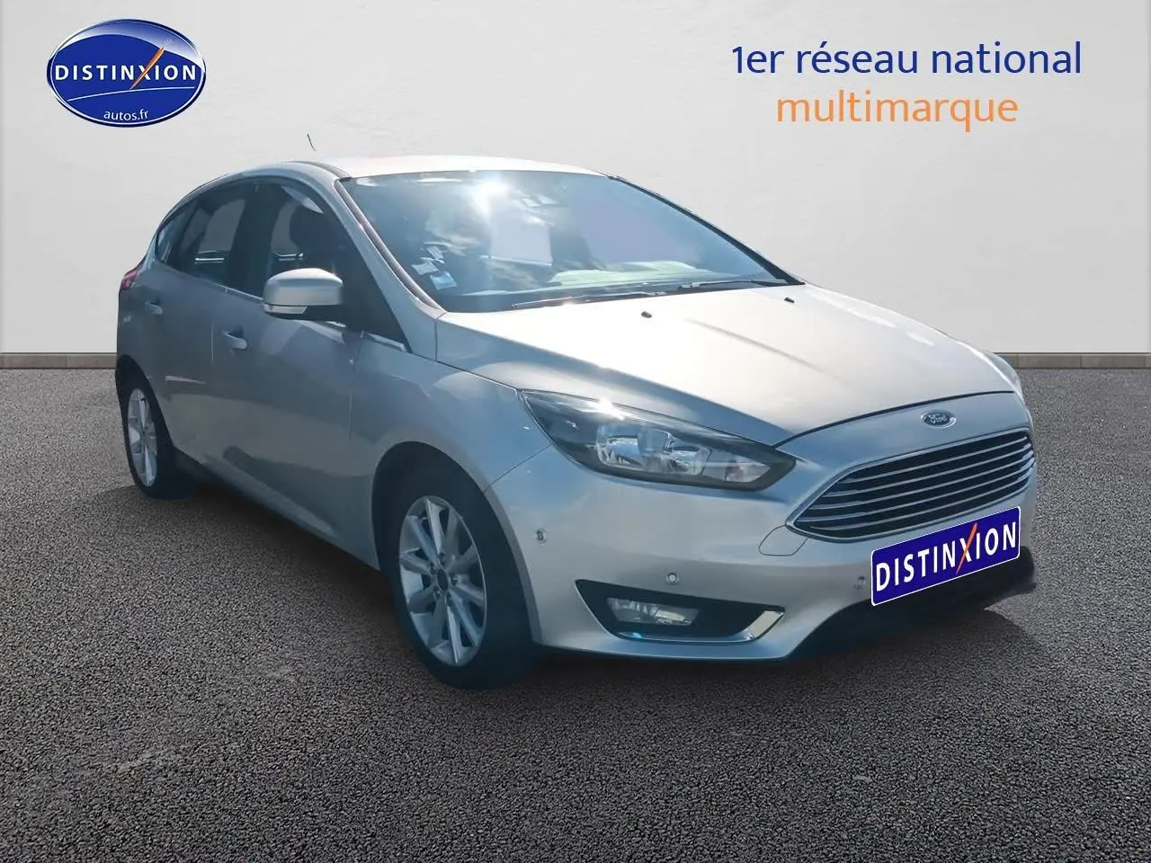 Ford Focus gris clair vue 3/4 avant droit avec calandre chromée et jantes alu sur fond neutre