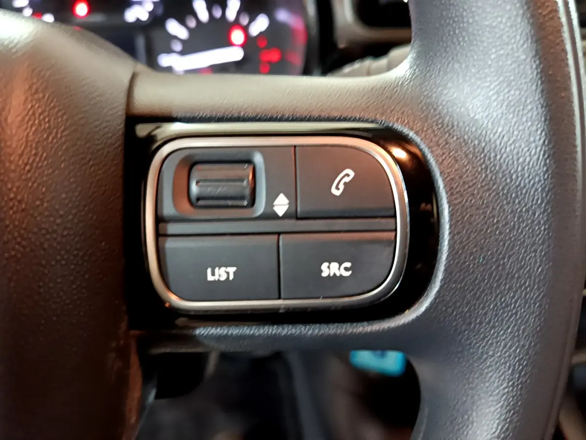 Gros plan sur les commandes noires du volant de la Citroën C3 beige, avec tableau de bord flou en arrière-plan.