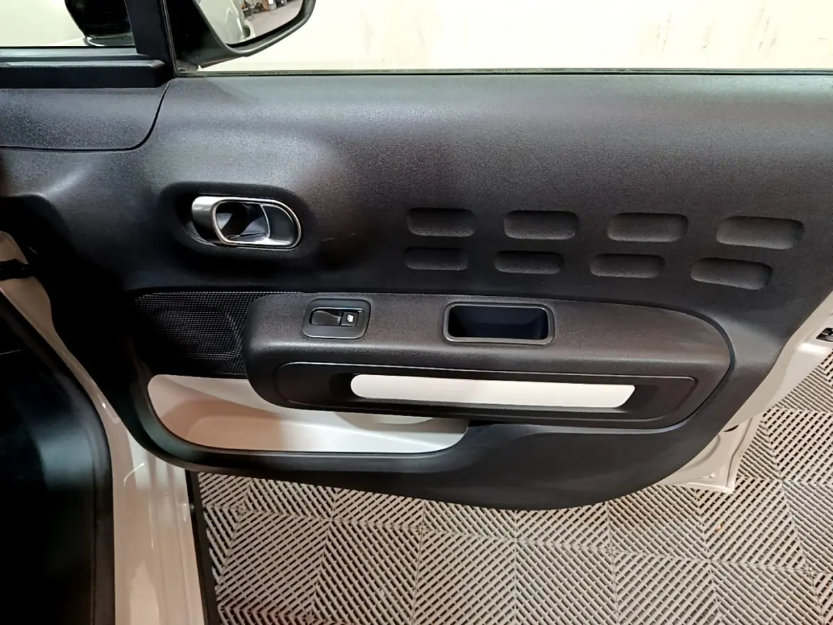 Vue rapprochée de la porte avant gauche beige de la Citroën C3 avec poignée intérieure chromée et panneau noir texturé.