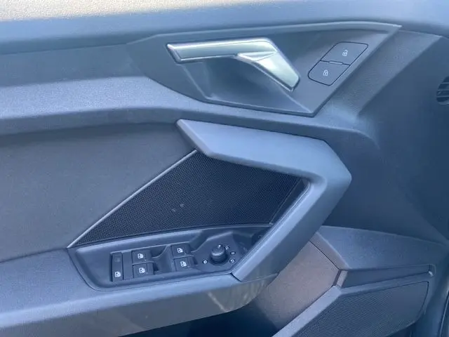 Détail de la porte intérieure côté conducteur de l'Audi A3 30 TDI 116 Business Line gris foncé, avec commandes électriques et poignée argentée.