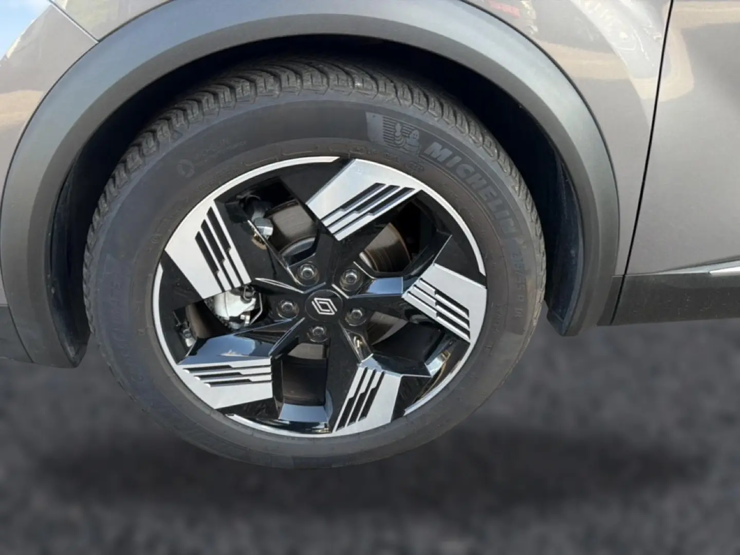Gros plan sur la roue avant droite d’une Renault Symbioz gris cassiopée avec jante noire et argent au design moderne.