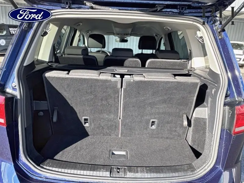 Coffre ouvert d'un Volkswagen Touran bleu Atlantique, montrant la troisième rangée de sièges en tissu noir.