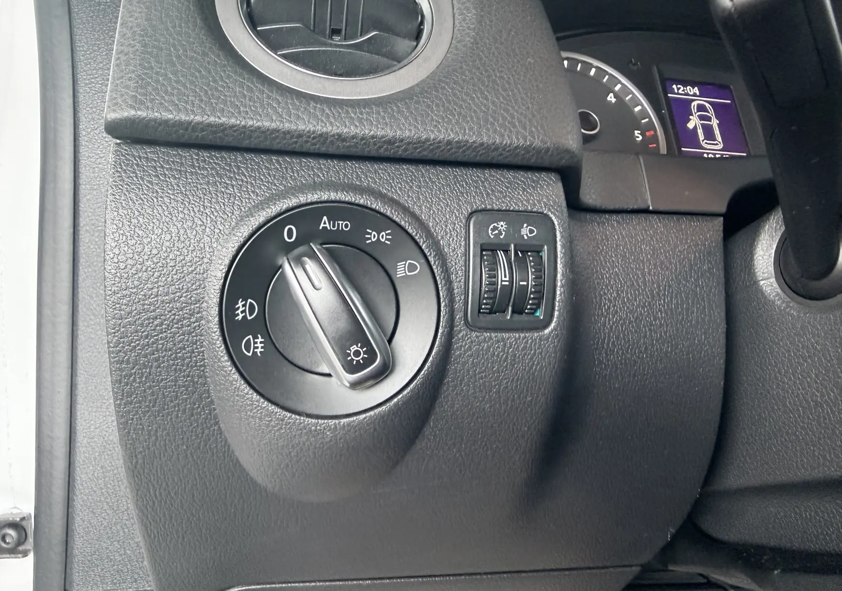 Gros plan sur le bouton de commande des phares à gauche du tableau de bord d’un Volkswagen Tiguan blanc de 2010.
