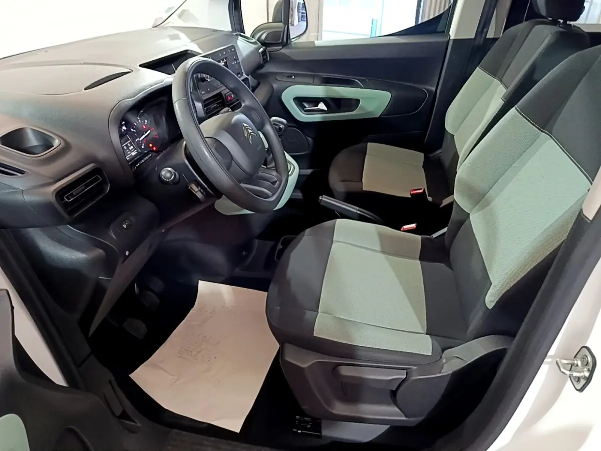 Vue intérieure côté conducteur du Citroën Berlingo blanc 2019, montrant le tableau de bord et sièges bicolores gris et noir.