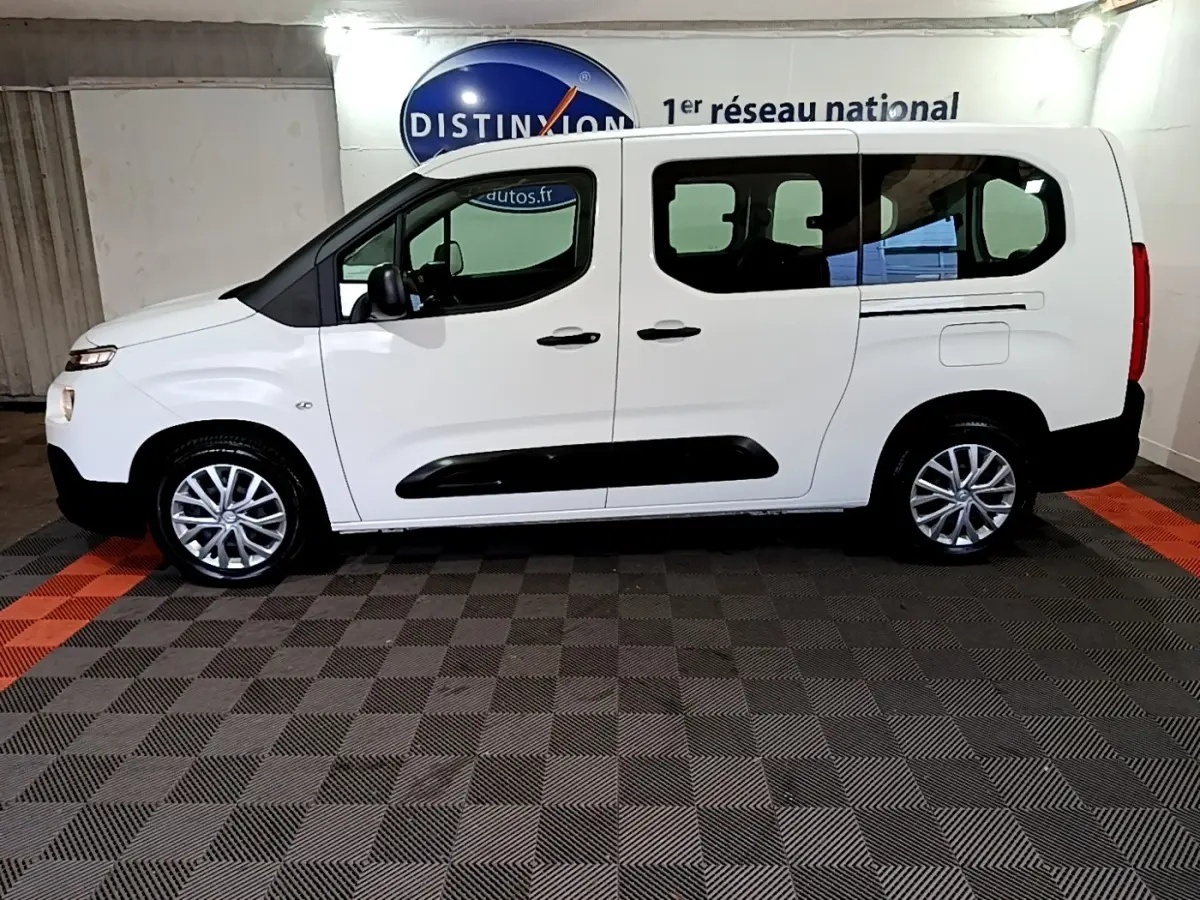 Vue de profil côté gauche d’un Citroën Berlingo XL blanc avec protections noires et jantes alliage en intérieur showroom.