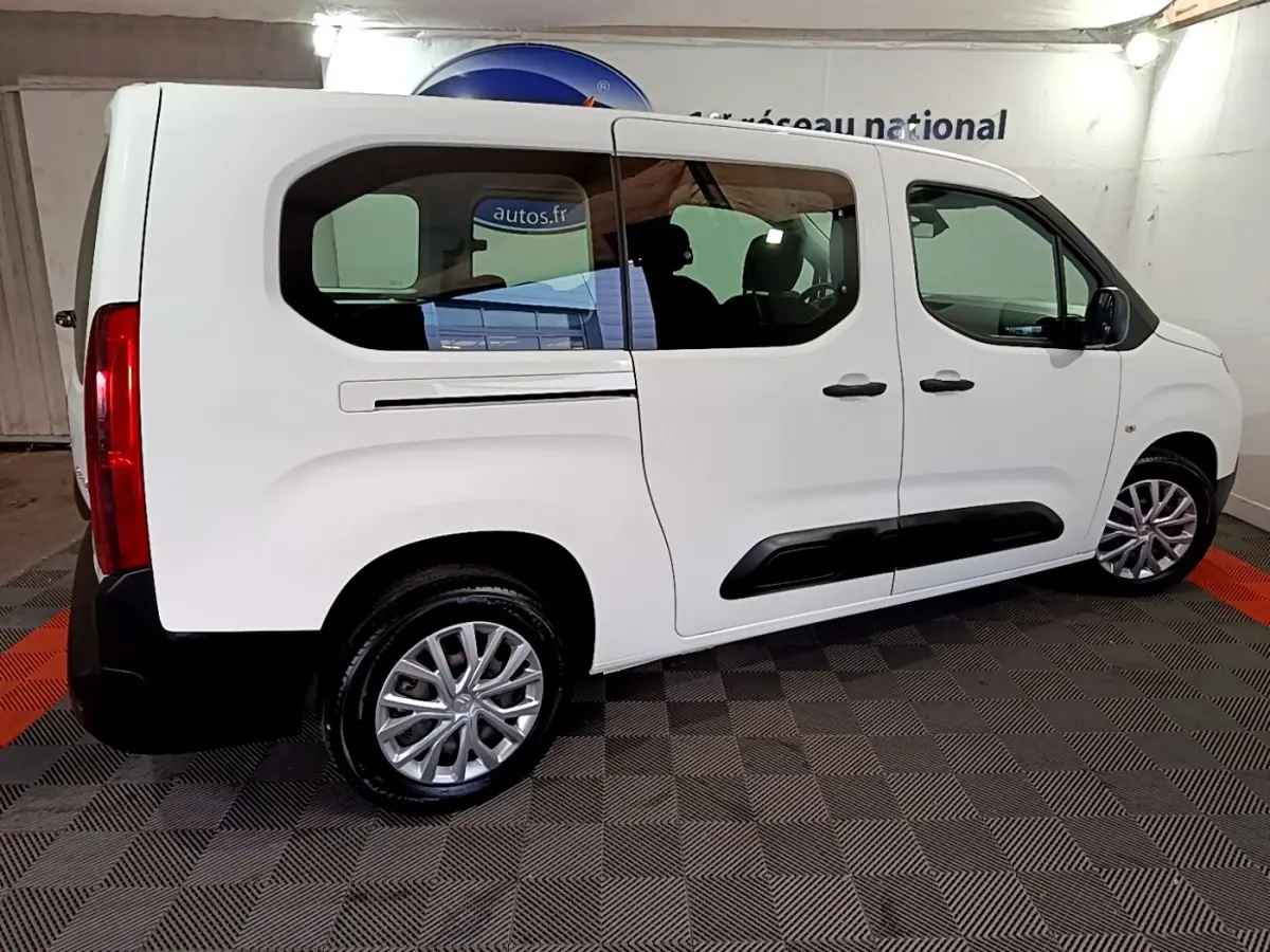Vue de profil côté droit d’un Citroën Berlingo XL blanc garé en intérieur, avec jantes alliage et protections noires sur les portières.