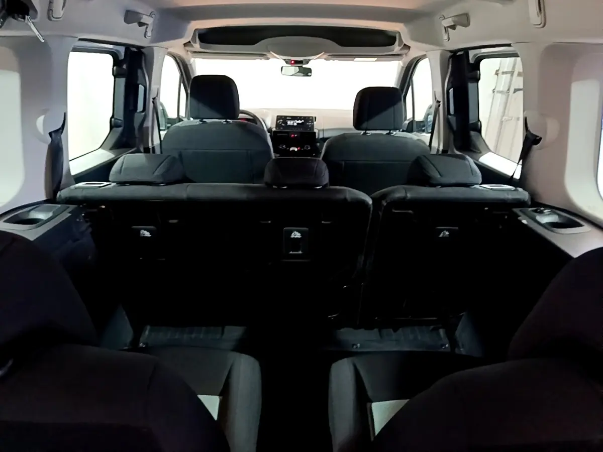 Vue intérieure arrière du Citroën Berlingo XL blanc, montrant les sièges arrière et le tableau de bord à l'avant.