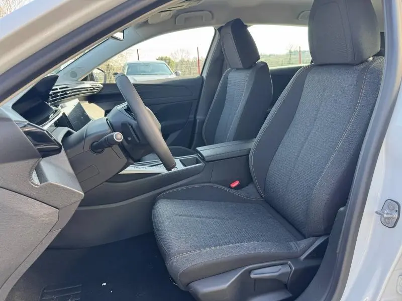 Intérieur de la Peugeot 308 blanc Okénite vu côté conducteur, sièges tissu gris et accoudoir central avec rangement.