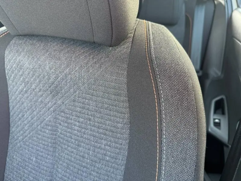 Gros plan sur le siège avant droit en tissu gris avec surpiqûres orange de la Peugeot 308 2025.