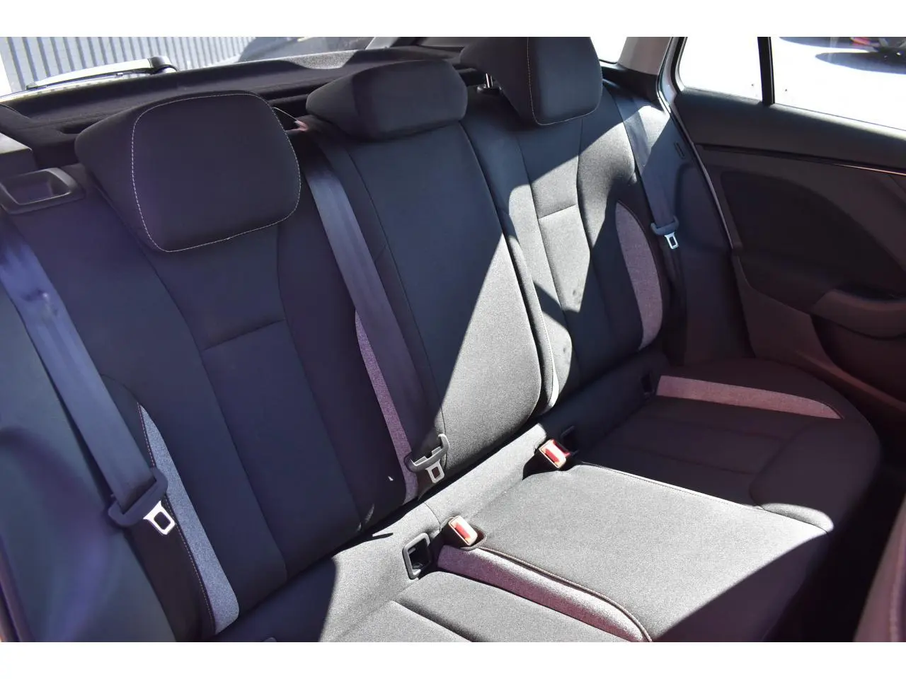 Vue latérale de la banquette arrière noire avec inserts gris et ceintures visibles dans une Skoda Scala blanche.