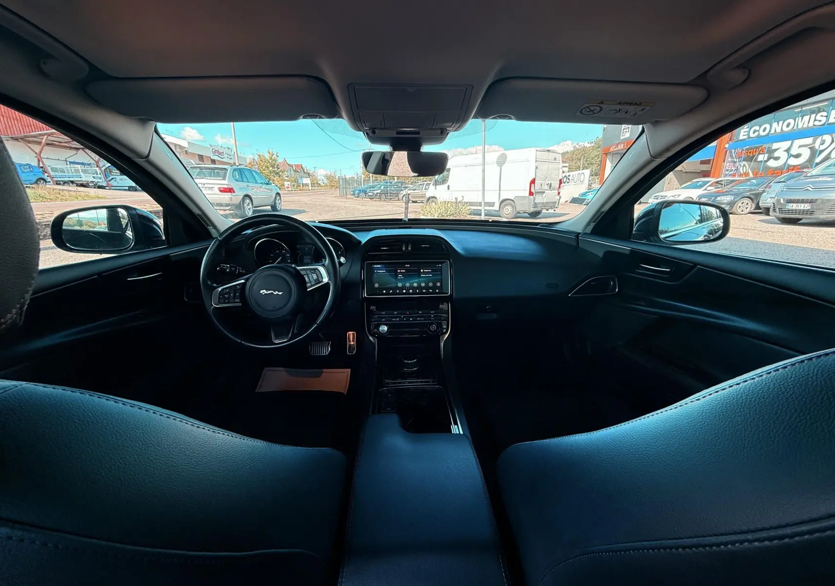 Vue intérieure avant de la Jaguar XE 2.0D 180CH Prestige 2019 avec tableau de bord et volant en cuir noir.