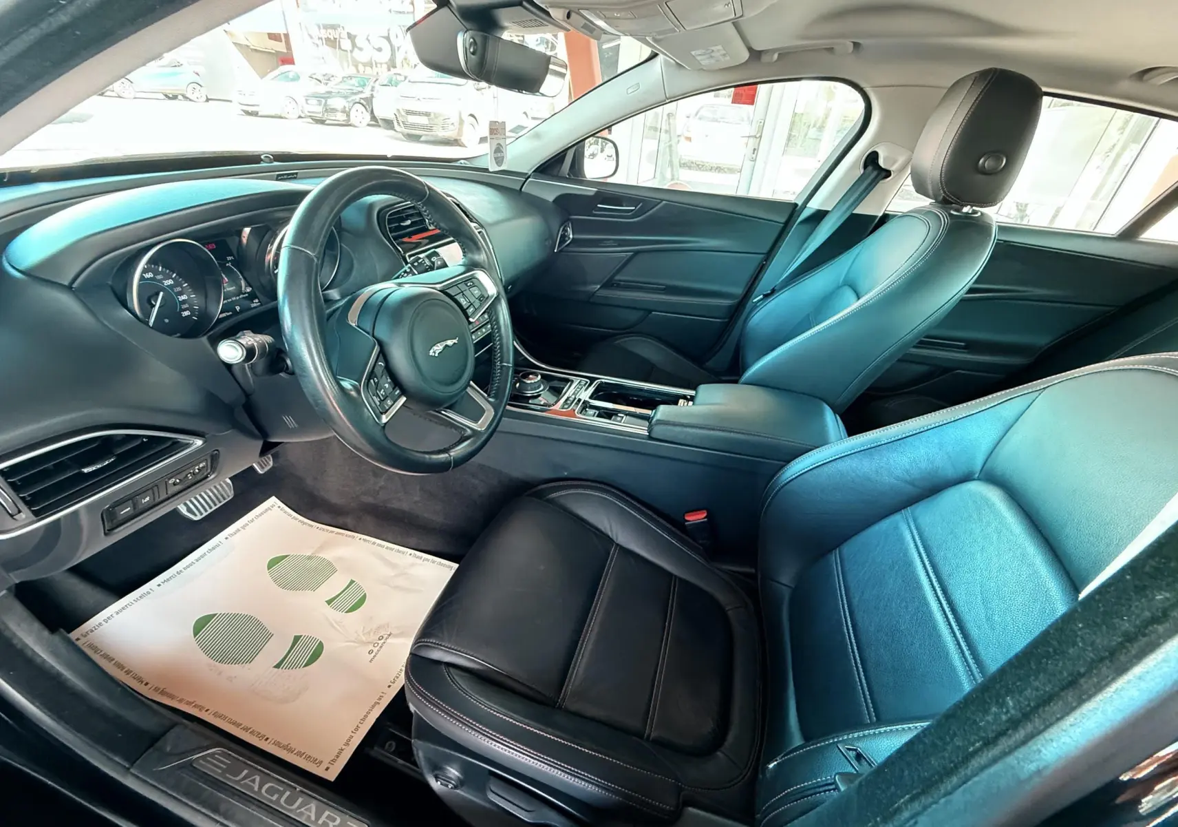 Intérieur noir cuir de la Jaguar XE 2.0D 180CH Prestige, vue côté conducteur avec tableau de bord et volant visibles.