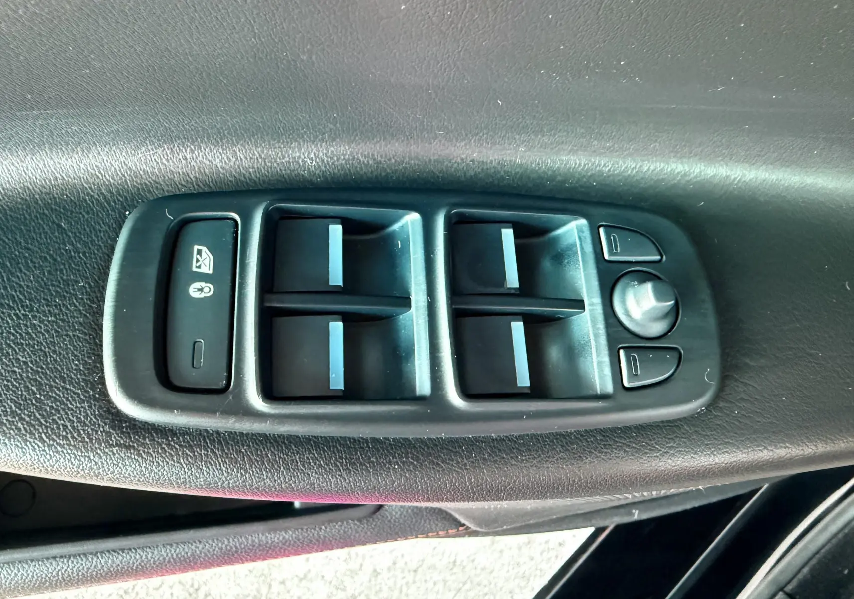 Panneau de commandes des vitres et rétroviseurs sur la porte intérieure d'une Jaguar XE noire, vue en gros plan.