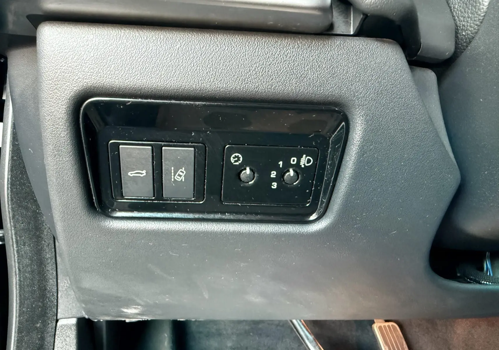 Gros plan sur les commandes de réglage des phares et ouverture du coffre côté gauche dans l'habitacle noir d'une Jaguar XE 2019.