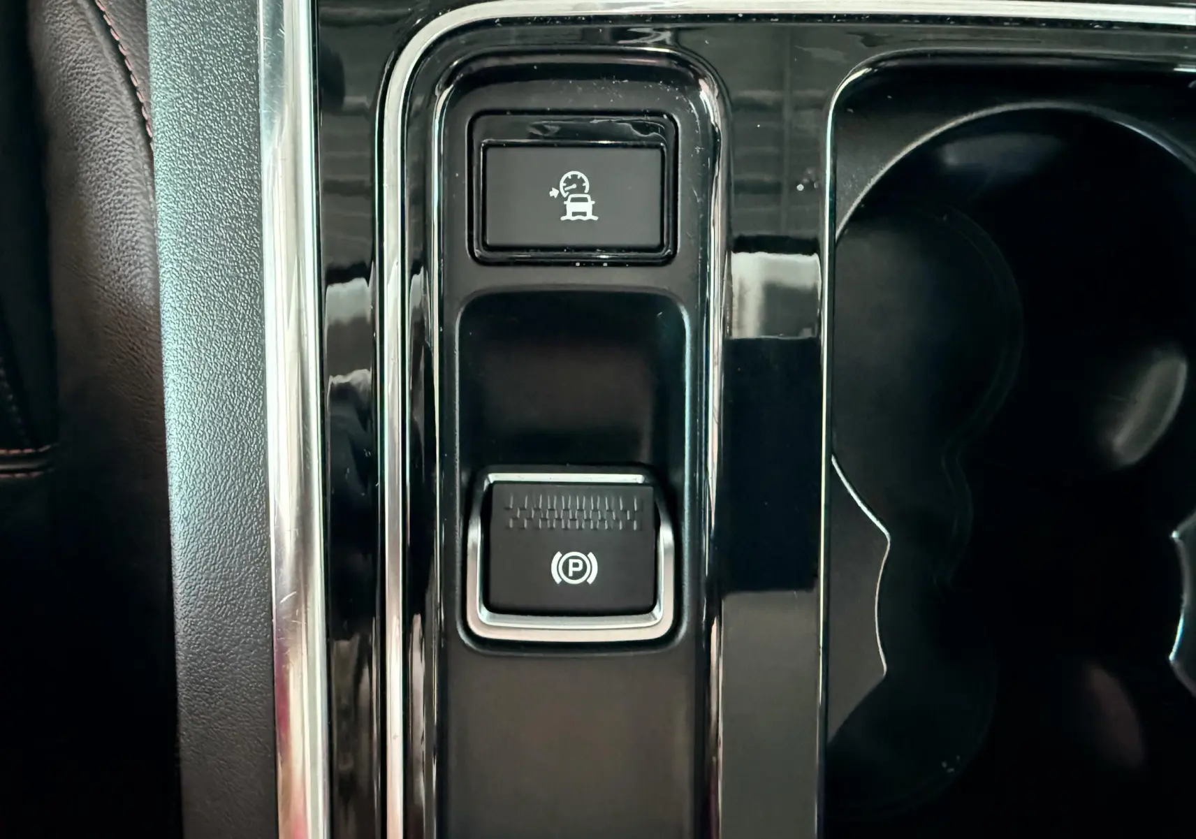 Gros plan sur la console centrale noire du Jaguar XE 2019 avec boutons de frein à main électronique et régulateur de vitesse adaptatif.