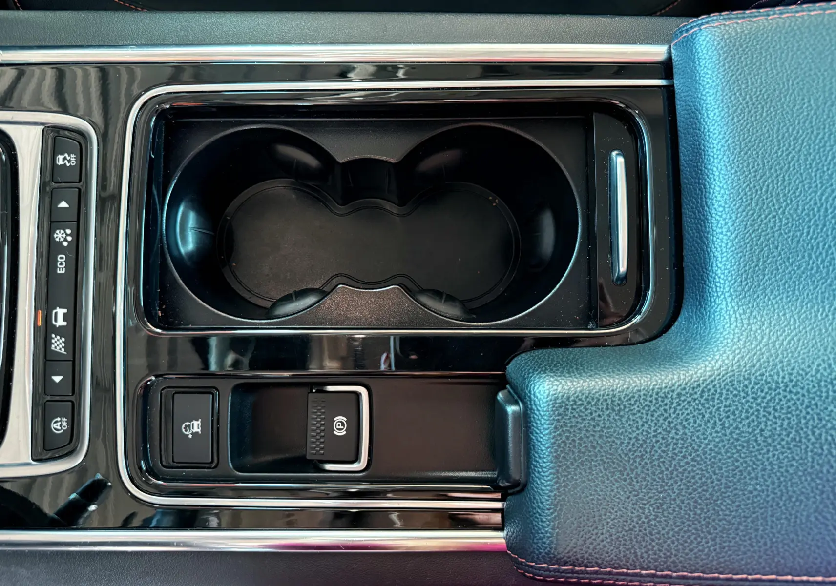 Gros plan sur la console centrale noire de la Jaguar XE 2.0D 180CH Prestige avec porte-gobelets et accoudoir cuir bleu.