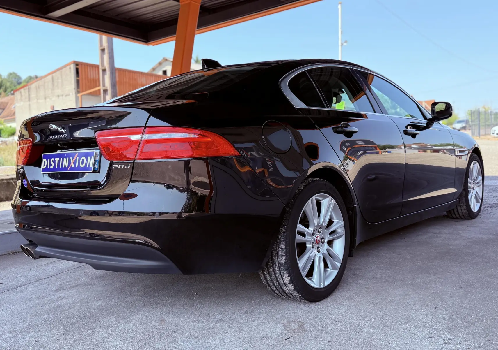 Vue 3/4 arrière droite d'une Jaguar XE noire brillante avec jantes argentées sous un abri extérieur.