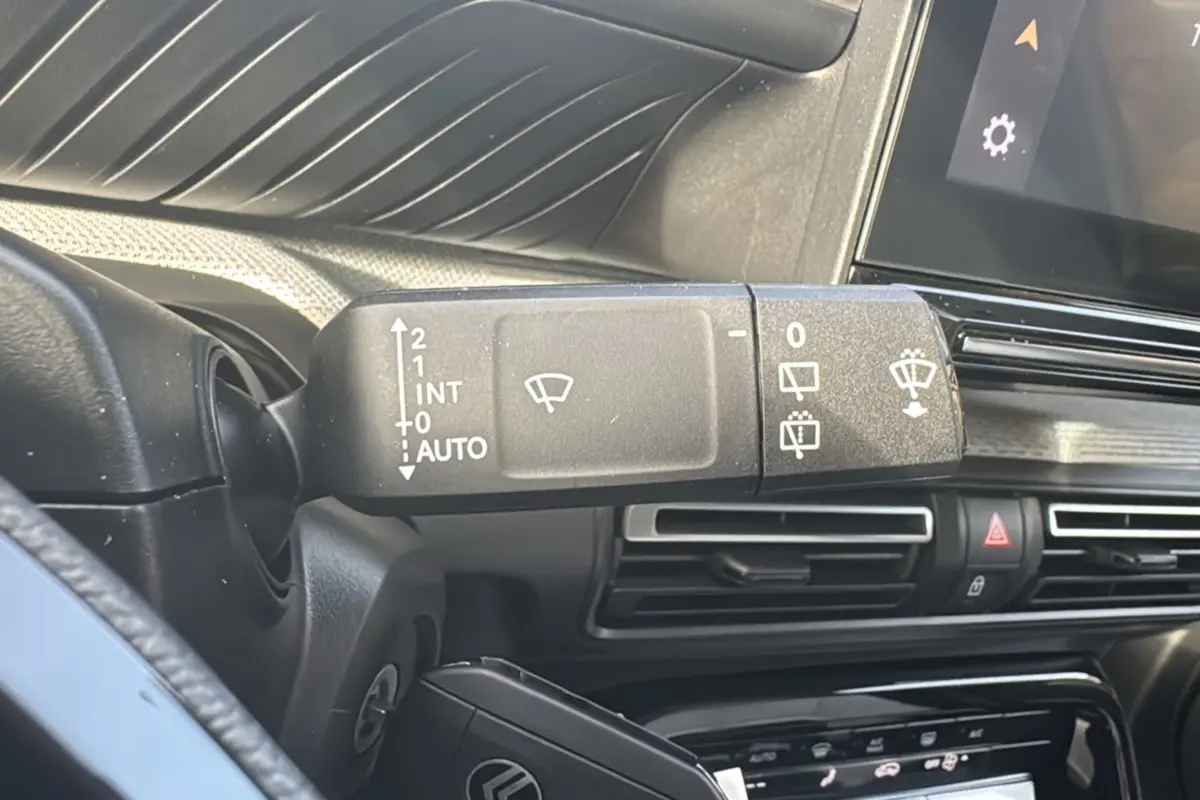 Gros plan sur la commande des essuie-glaces à gauche du volant dans l'habitacle du Citroën C3 Aircross blanc banquise.